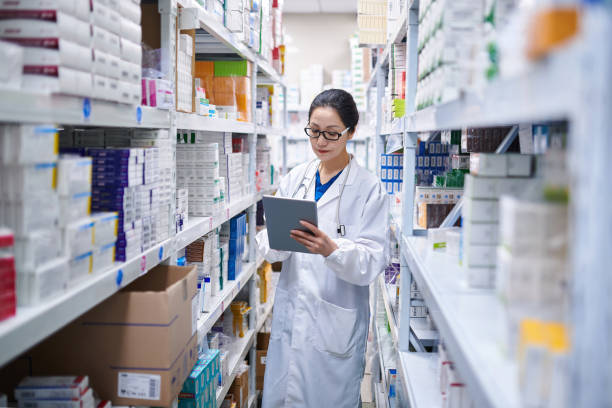 Side view of one asia female pharmacist using digital tablet while taking inventory at pharmacy warehouse.